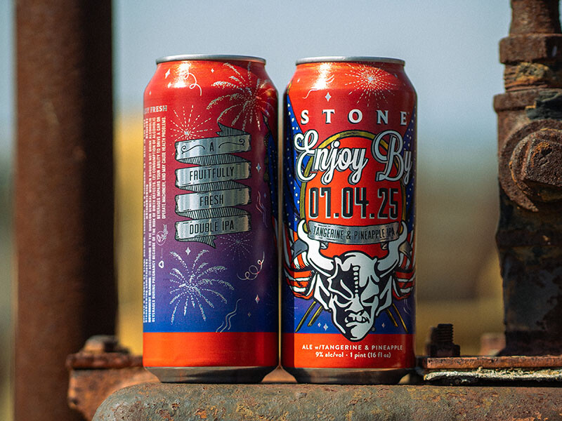 two cans of Stone Enjoy By 07.04.25 Tangerine & Pineapple IPA next to each other on pipes