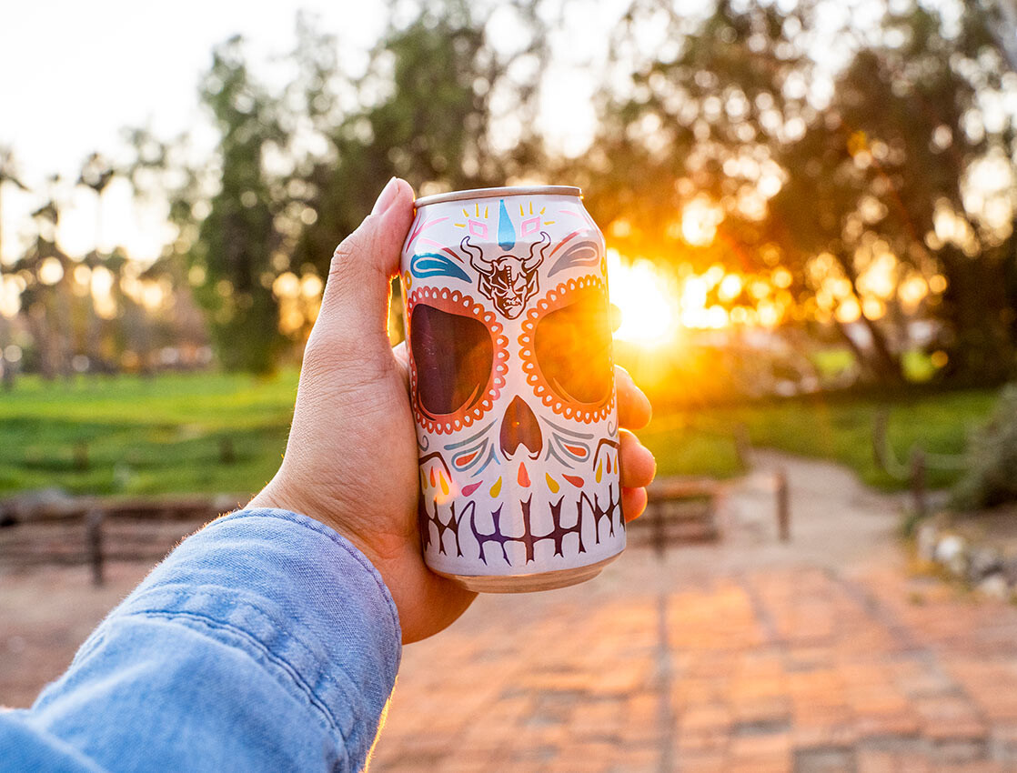 hand holding a can of buenaveza in front of the sunset