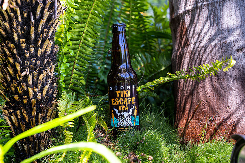 Stone Tiki Escape IPA bottle between palm trees